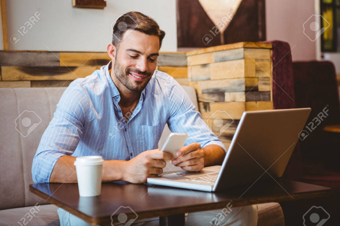 42515465-Smiling-businessman-sending-a-text-message-with-laptop-beside-Stock-Photo.jpg